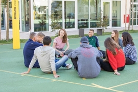 Grupper junger Mensch sitzen mit Erzieher auf dem Boden des Sportplatzes und unterhalten sich.