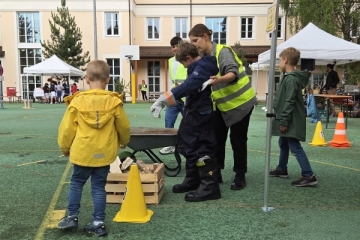 3 Kinder machen sich bereit, den Hindernisparcour mit einer Schubkarre zu durchfahren. Eine Betreuerin in Warnweste hilft dabei.