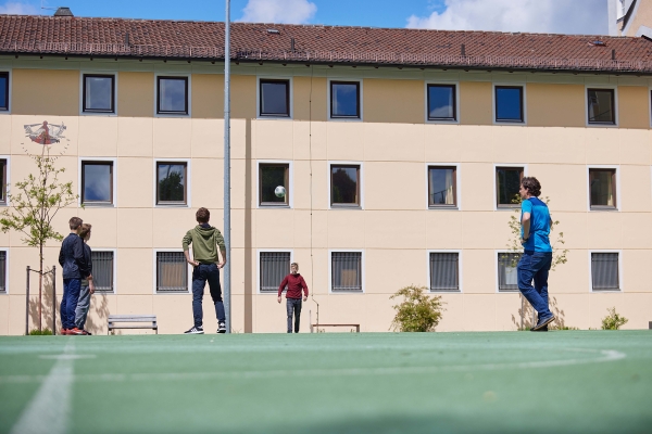 Erzieher spielt mit Kindern aus dem Oratorium auf dem Sportplatz Fußball