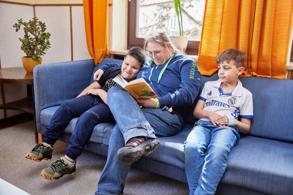 Erzieherin liest mit zwei Jungen ein Buch in der Couchecke