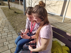 Freiwillige sitzt mit einer jungen Frau aus der Ukraine draußen auf einer Sitzbank kommuniziert mit ihr über Google-Translator.