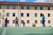 Erzieher spielt mit Kindern aus dem Oratorium auf dem Sportplatz Fußball